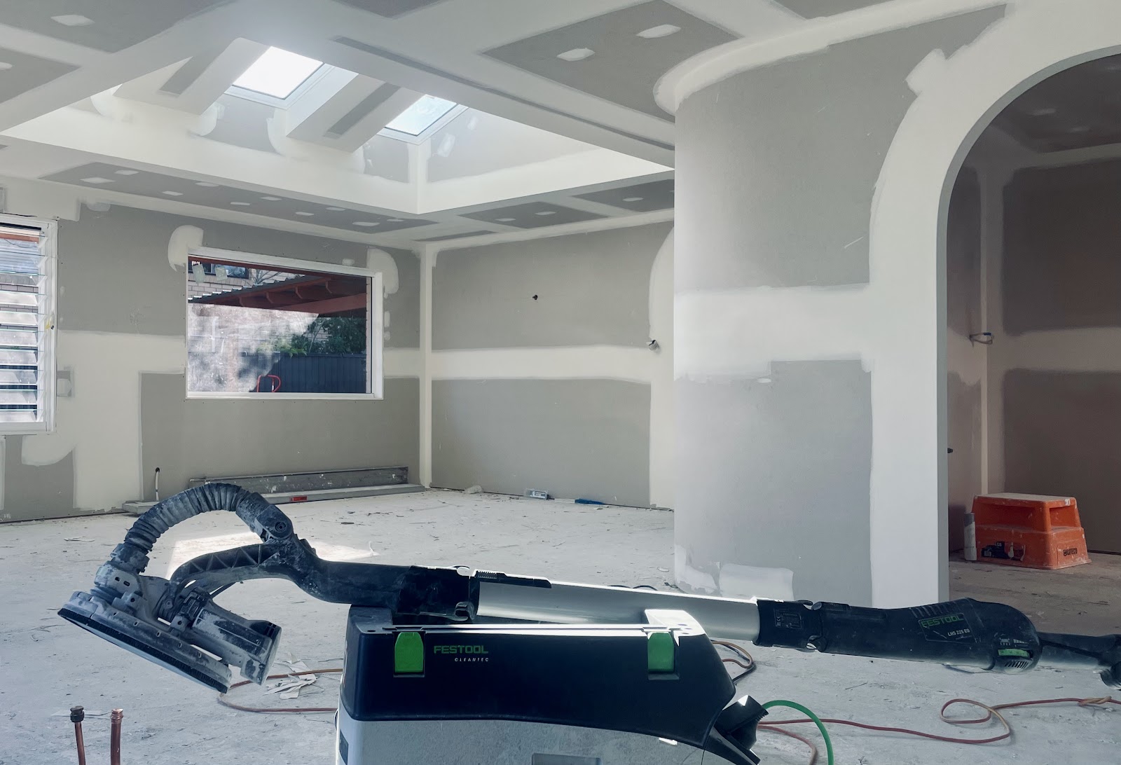 Open-plan room with skylights, a curved wall and an arch, freshly set, with a dust-extracted sander in the foreground