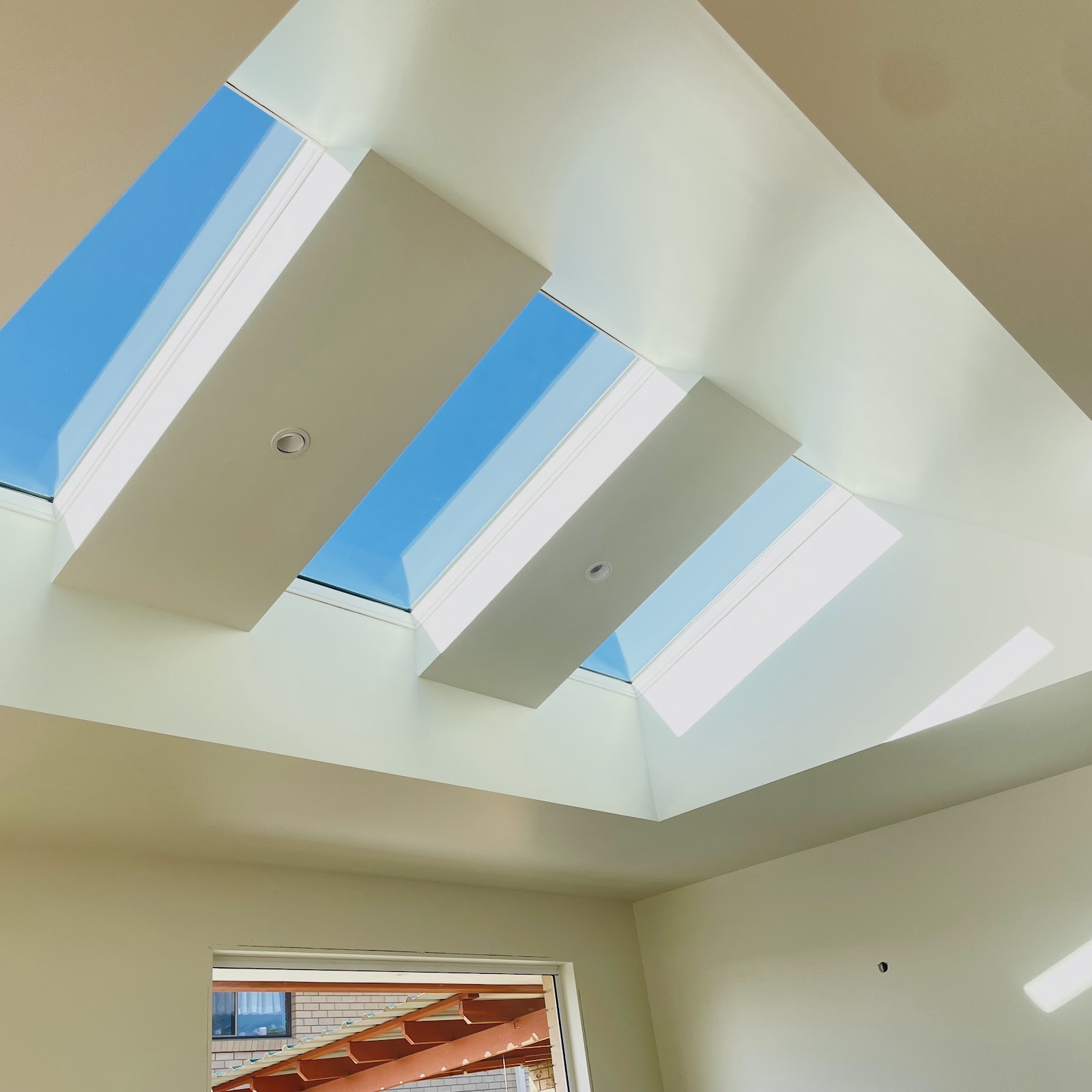 Finished white ceiling with three skylight wells and blue sky above